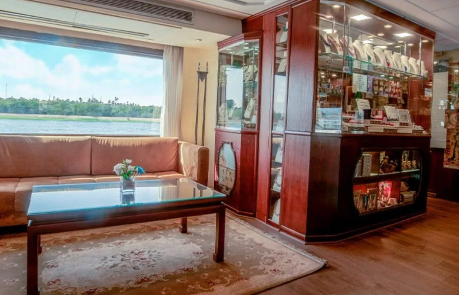 The on-board gift shop and lounge on the Ms Nile Goddess Nile Cruise, featuring display cases and comfortable seating with a view of the Nile.
