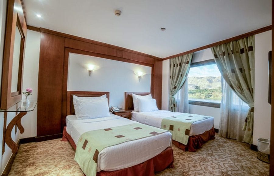 A comfortable twin-bed cabin on the Ms Nile Goddess Nile Cruise with a large window overlooking the Nile River and mountains.