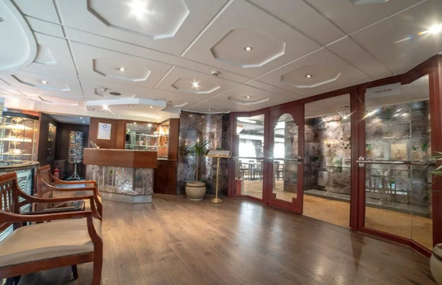 The sophisticated lobby of the Sonesta Nile Goddess Cruise​ with a polished wooden reception desk and a staircase leading to the upper deck.