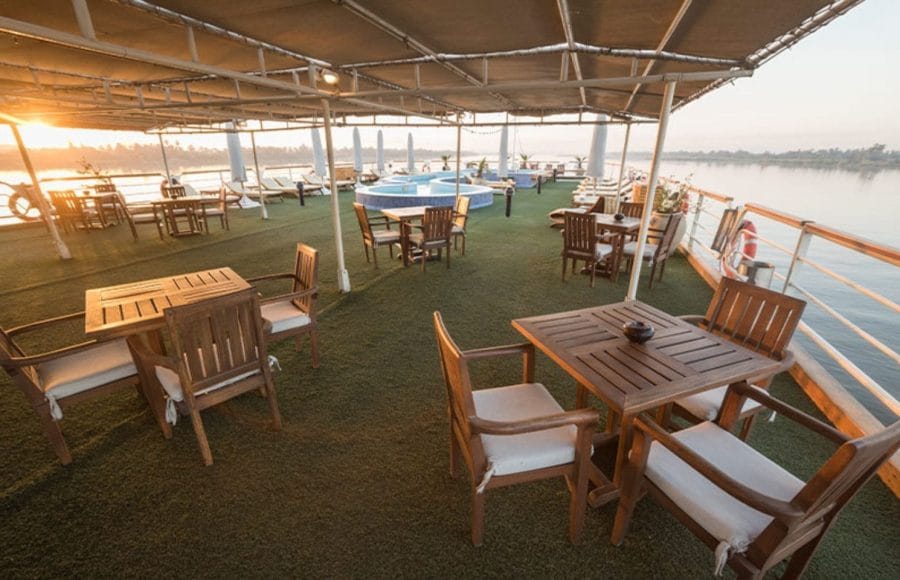 Guests dining and lounging on the sun deck of the MS Nile Goddess Nile Cruise as the sun sets over the river.