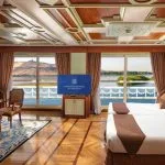 A luxurious twin-bed cabin aboard the MS Sonesta St. George Nile Cruise ship, featuring panoramic windows with stunning river views.