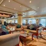 The elegant lounge on the MS Sonesta St George Nile Cruise, featuring plush sofas, comfortable armchairs, and large windows with scenic views, perfect for relaxing and socializing.