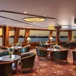 The elegant main restaurant on the MS Sonesta St George Nile Cruise, featuring comfortable seating and panoramic windows with a beautiful sunset view over the Nile River.
