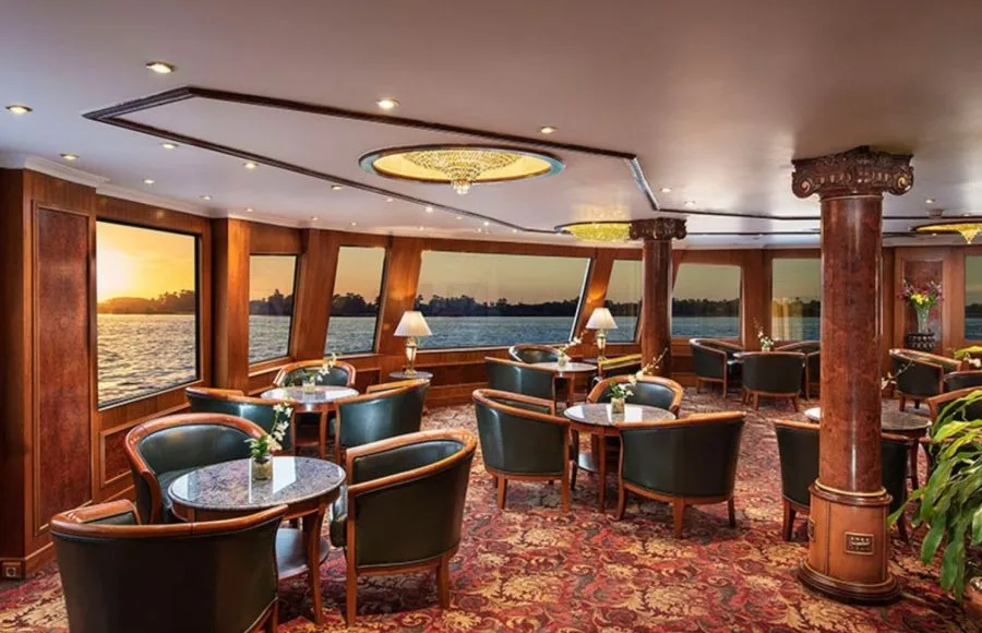 The elegant main restaurant on the MS Sonesta St George Nile Cruise, featuring comfortable seating and panoramic windows with a beautiful sunset view over the Nile River.