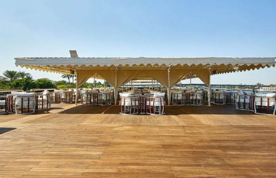 The sunny upper deck of the Ms Sonesta St George Nile Cruise ship with covered seating areas and a wooden floor.