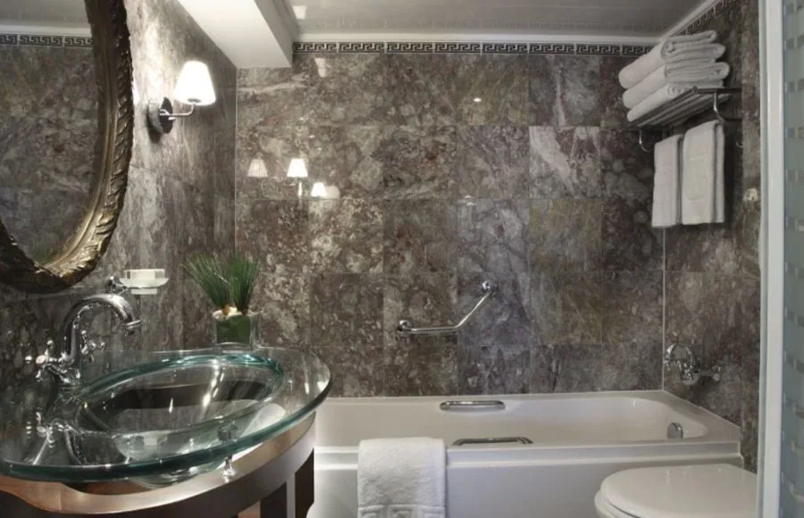 A luxurious and modern bathroom on the Sonesta Star Goddess Nile cruise ship, with a sleek glass basin, bathtub, and stylish marble-patterned walls.