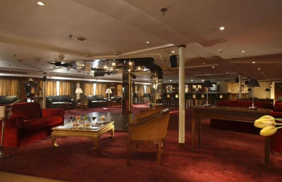 An elegant and sophisticated dining lounge on the Sonesta Star Goddess Nile cruise ship, with red velvet couches, a bar, and low tables with drinks.