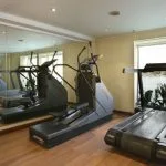 The onboard gymnasium of the Sonesta Star Goddess Nile cruise ship, featuring a treadmill, an elliptical machine, and large windows with a scenic view of the Nile River.