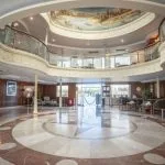 The grand and elegant lobby of the Sonesta Star Goddess Nile cruise ship, featuring a high ceiling with a beautiful mural and a sweeping staircase.