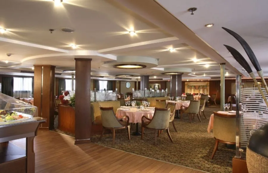 The elegant and spacious restaurant on the Sonesta Star Goddess Nile cruise ship, set with tables and a buffet station for a delightful dining experience.