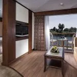A spacious suite on the Sonesta Star Goddess Nile cruise ship, featuring a comfortable bed, a separate sitting area, and a private balcony overlooking the Nile River.