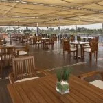 An inviting outdoor dining area on the sundeck of the Sonesta Star Goddess Nile cruise ship, with wooden tables and chairs shaded by a canopy.