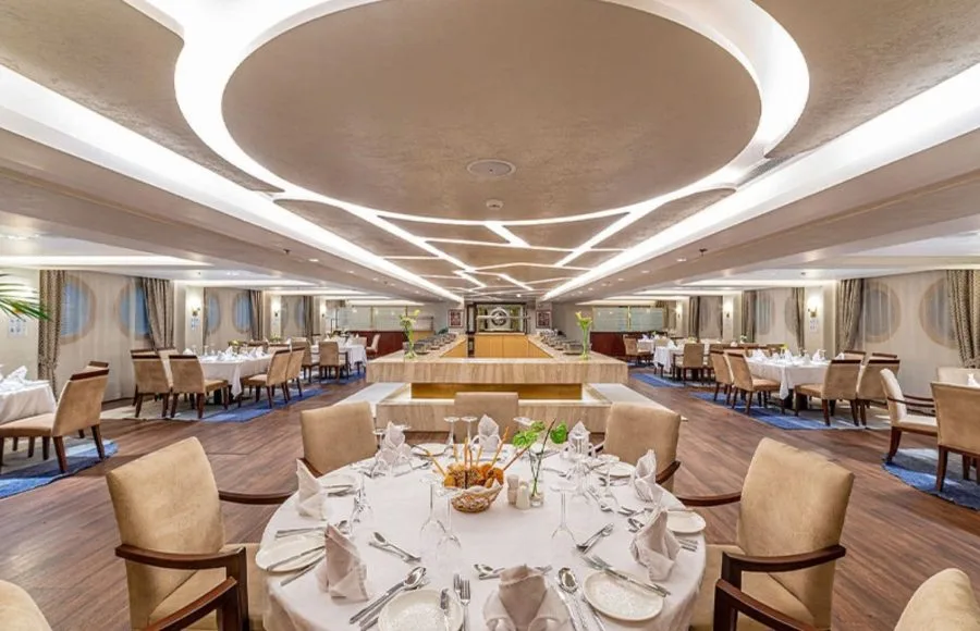 The elegant and spacious dining room on the Sonesta Sun Goddess Nile cruise ship, set with tables and chairs ready for a delicious meal.
