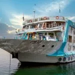 The elegant Sonesta Sun Goddess Nile cruise ship, a Sonesta Sun Goddess Nile River Cruise, is shown sailing majestically on the Nile River under a clear sky.