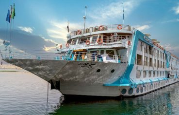 The elegant Sonesta Sun Goddess Nile cruise ship, a Sonesta Sun Goddess Nile River Cruise, is shown sailing majestically on the Nile River under a clear sky.
