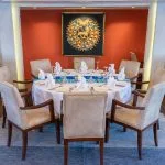 An elegantly set dining table in the restaurant of the Sonesta Sun Goddess Nile River Cruise, featuring a decorative centerpiece and comfortable chairs.