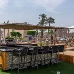 The sunny deck bar on the Sonesta Sun Goddess Nile cruise ship, with comfortable stools and a view of ancient Egyptian ruins in the distance.