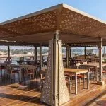 Guests relaxing on the sunny top deck of the Sonesta Sun Goddess Nile cruise ship, enjoying a meal under a patterned canopy with views of the Nile River.