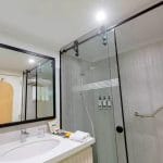 The clean and modern guest bathroom on the MS Tamr Nile Cruise features a bright vanity sink and a glass-enclosed shower with contemporary black fixtures and white tiling