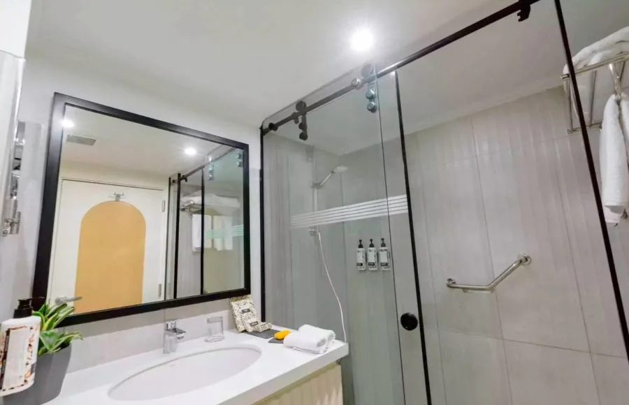 The clean and modern guest bathroom on the MS Tamr Nile Cruise features a bright vanity sink and a glass-enclosed shower with contemporary black fixtures and white tiling
