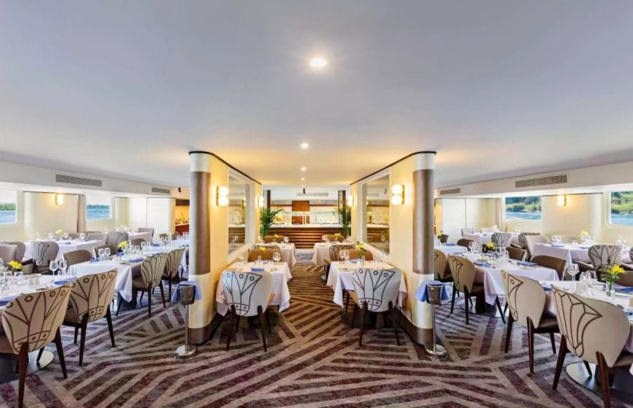 The elegant dining room of the Tamr Henna Nile Cruise Ship features beautifully set tables with crisp white linens and large windows offering scenic views of the Nile River