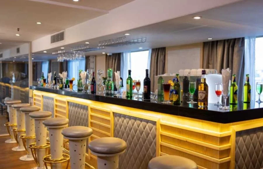 Sleek, modern bar on a ship with cushioned stools, backlighting, and liquor bottles on the counter.