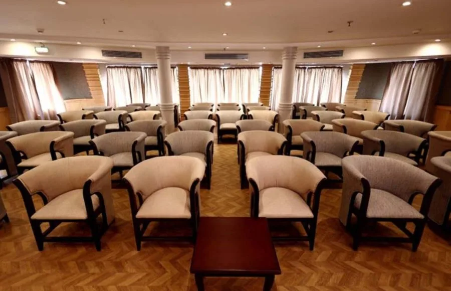 Symmetrical layout of numerous cushioned armchairs in an indoor lounge on a ship.
