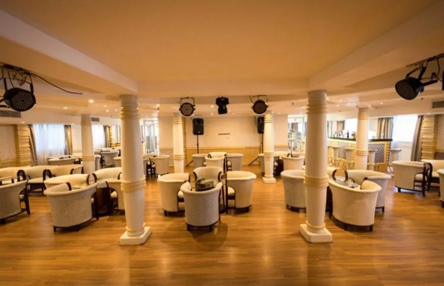 Symmetrical layout of cushioned armchairs in a ship's main lounge with curtains covering the windows.