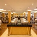 Formal dining room on a ship with round and rectangular tables, high-backed chairs, and wooden columns.