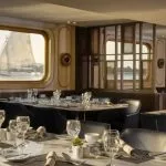 The elegant dining room of the MS Tulip Nile Cruise with set tables and a large window providing an engaging view of a felucca sailing on the Nile River.