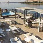 An elevated view of the sundeck of the MS Tulip Nile Cruise, featuring a pool, loungers, and shaded seating with a river view.