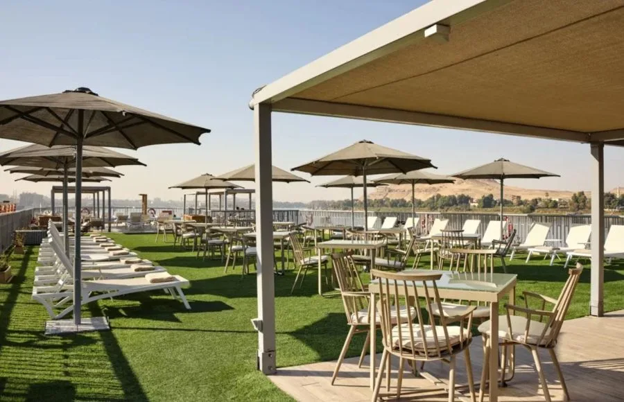 The lush sundeck of the MS Tulip Nile Cruise features comfortable dining tables, umbrellas, and sun loungers set on artificial grass with captivating river views.