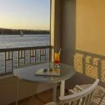 A private terrace view from the MS Tulip Nile Cruise at sunset, featuring a cocktail and sunglasses overlooking the beautiful Nile River.