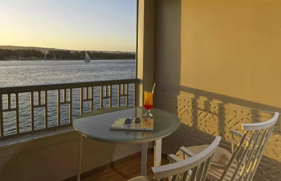 A private terrace view from the MS Tulip Nile Cruise at sunset, featuring a cocktail and sunglasses overlooking the beautiful Nile River.