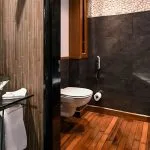 A modern and stylish bathroom onboard the Moondance Nile Cruise, featuring a sleek glass basin, a contemporary toilet, and a spacious shower area with natural wood flooring and elegant stone tiling.