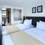 A spacious and modern twin-bed cabin on the Moondance Nile Cruise, featuring clean white bedding, contemporary decor, and an en-suite bathroom with a view of the river.