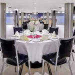 The elegant and spacious restaurant on the Moondance Nile Cruise, featuring a round table with a pristine white tablecloth, black chairs, and a buffet area in the background.