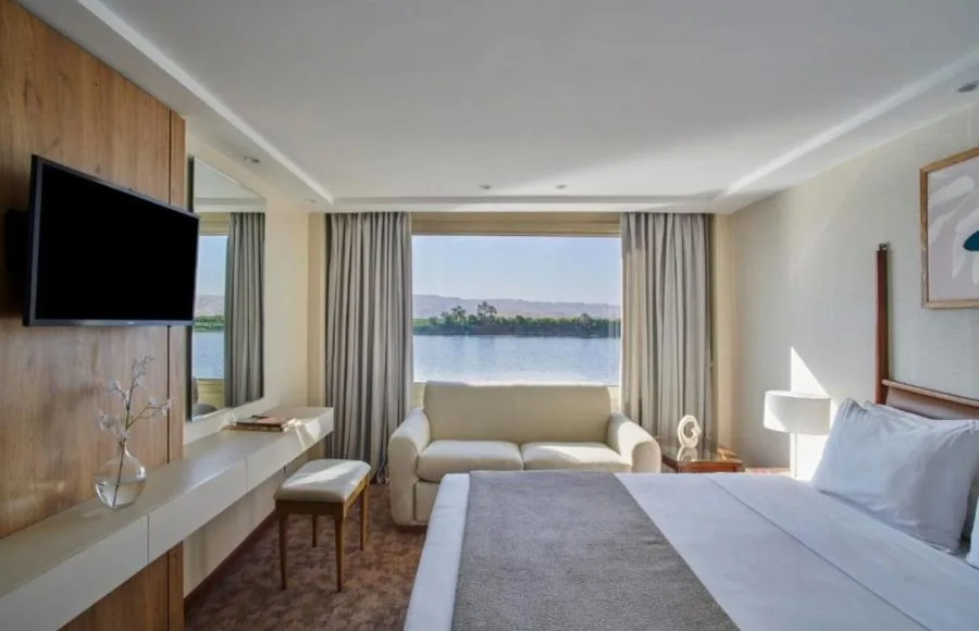 A spacious suite on the Mövenpick MS Royal Lotus Nile Cruise with a large bed, sofa, and stunning river views.