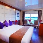 A cozy double cabin on the Blue Shadow 4, with a large bed, seating area, and a view of the Nile River.