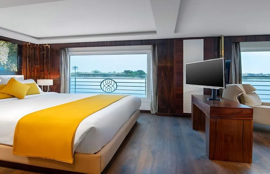 A luxurious suite on the Sindbad Nile cruise, with a comfortable bed, modern television, and a large window offering spectacular views of the river.