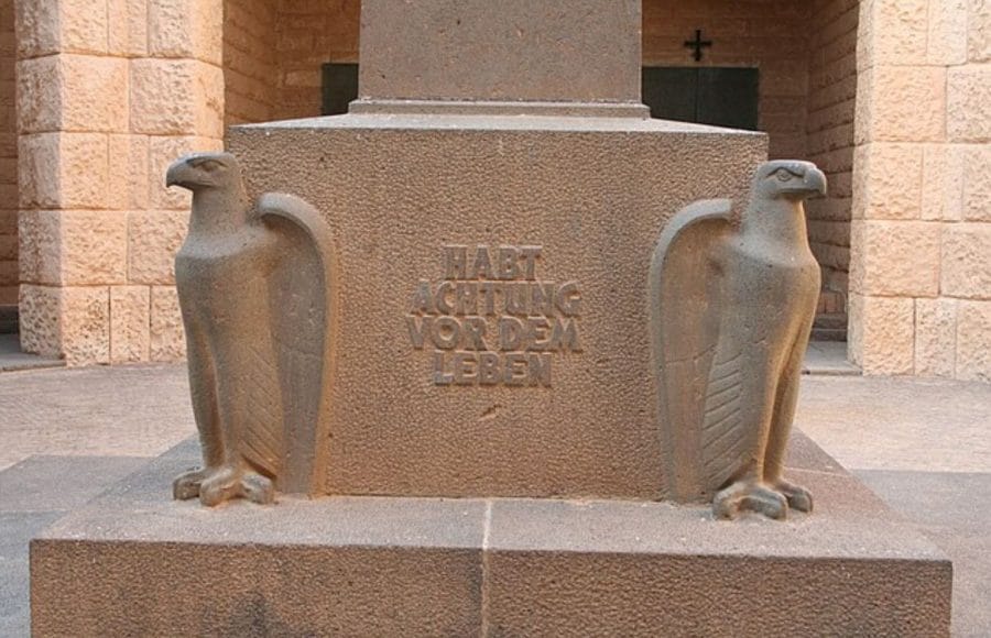 A close-up view of the stone base and eagle statues at The German War Memorial in El Alamein, featuring the German inscription, "HABT ACHTUNG VORDEM LEBEN" (Respect Life).