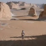 A man standing in the vast, sandy landscape of Agabat Valley, surrounded by white chalk rock formations.