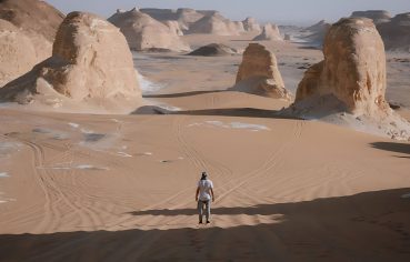 A man standing in the vast, sandy landscape of Agabat Valley, surrounded by white chalk rock formations.