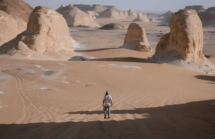 A man standing in the vast, sandy landscape of Agabat Valley, surrounded by white chalk rock formations.