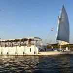 A traditional two-masted wooden sailboat, the Abundance Dahabiya, cruising the Nile River with open sails