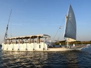 A traditional two-masted wooden sailboat, the Abundance Dahabiya, cruising the Nile River with open sails
