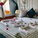 A hotel room bed decorated with towel art and red rose petals.