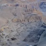 A wide Aerial view of Deir el-Medina Valley of the Workers, showing the extensive ruins of the ancient village nestled against the rugged desert cliffs of the Theban Necropolis.