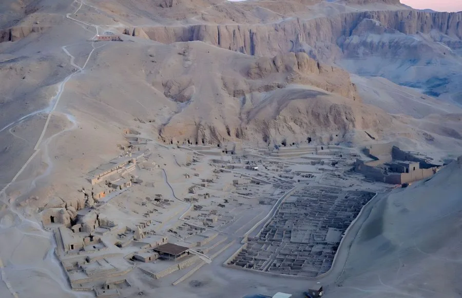 A wide Aerial view of Deir el-Medina Valley of the Workers, showing the extensive ruins of the ancient village nestled against the rugged desert cliffs of the Theban Necropolis.