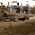 An interior display at the Alamein Military Museum, showing a recreated sandbag bunker with mannequins in military uniform wielding a machine gun, with a visitor taking a photo in the background.